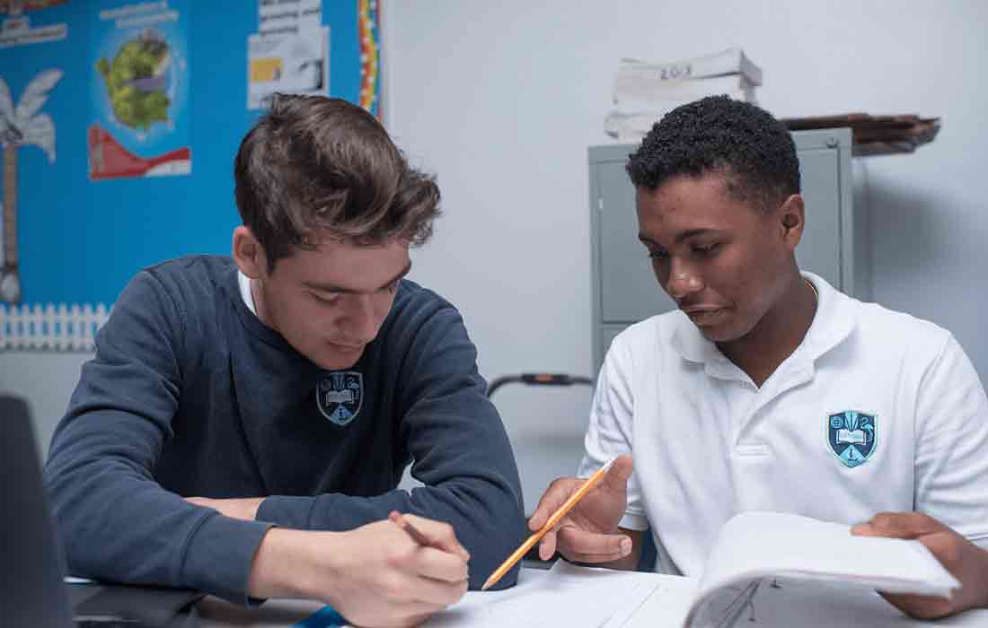Two students working together at table with books