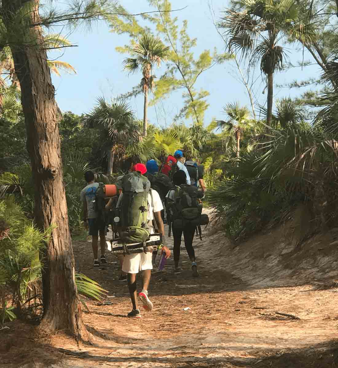 Students wearing backpack hiking on trail in tropical woods